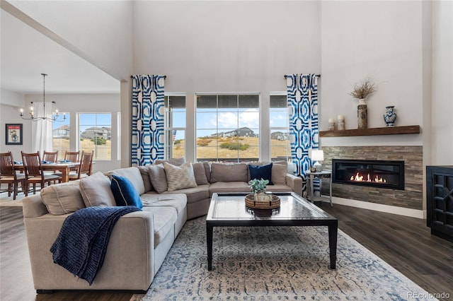 living room with a stone fireplace, a high ceiling, a notable chandelier, and hardwood / wood-style flooring