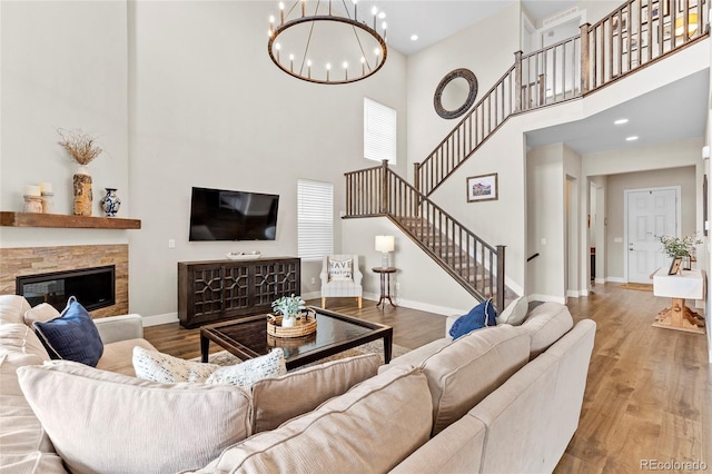 living room featuring hardwood / wood-style flooring, a stone fireplace, a high ceiling, and a chandelier