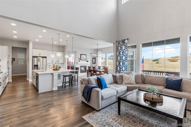 living area featuring dark wood-style flooring, recessed lighting, a high ceiling, a chandelier, and baseboards