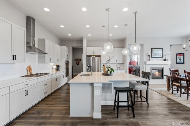 kitchen featuring appliances with stainless steel finishes, white cabinetry, sink, a kitchen island with sink, and wall chimney exhaust hood