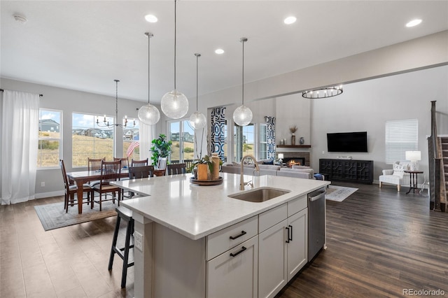 kitchen featuring a sink, white cabinetry, open floor plan, hanging light fixtures, and a center island with sink