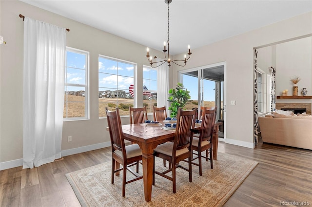 dining room featuring a notable chandelier, a fireplace, baseboards, and wood finished floors