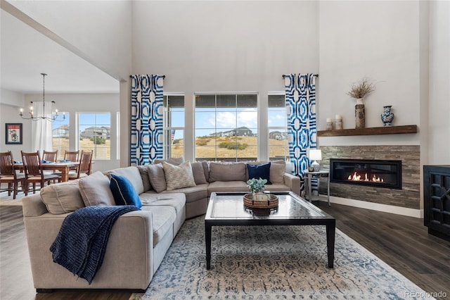 living area featuring a towering ceiling, a notable chandelier, wood finished floors, and a stone fireplace