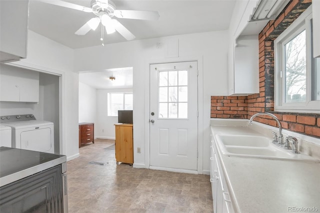 kitchen featuring sink, ceiling fan, brick wall, washer and clothes dryer, and white cabinets