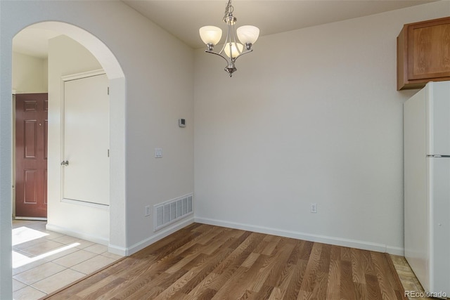 unfurnished dining area featuring arched walkways, light wood-style flooring, visible vents, and baseboards