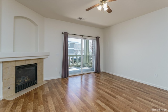 unfurnished living room with baseboards, visible vents, a ceiling fan, a tiled fireplace, and light wood-style floors