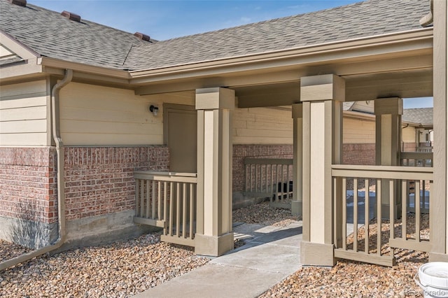 doorway to property featuring brick siding and roof with shingles