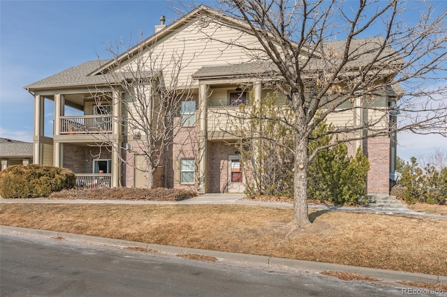 view of front of property featuring a balcony, a chimney, and a shingled roof