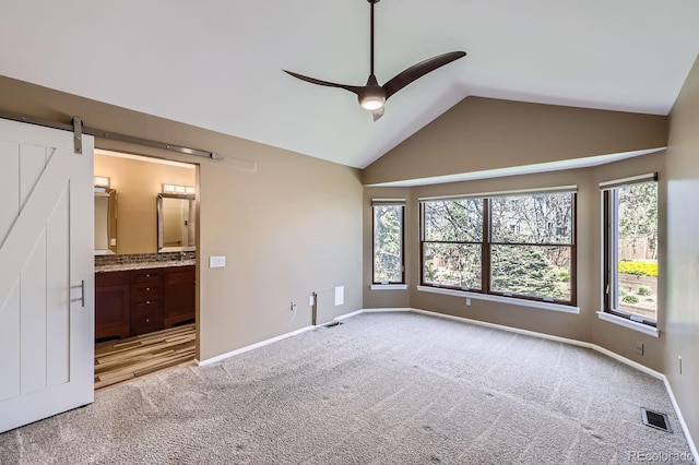 9916 Spring Hill Ln, Highlands Ranch, CO 80129 - unfurnished bedroom with light colored carpet, lofted ceiling, a barn door, connected bathroom, and ceiling fan
