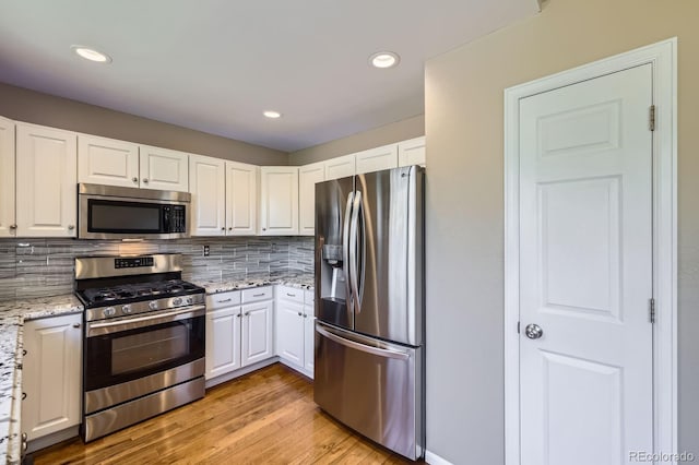 9916 Spring Hill Ln, Highlands Ranch, CO 80129 - kitchen featuring appliances with stainless steel finishes, white cabinets, light wood-style floors, decorative backsplash, and light stone countertops