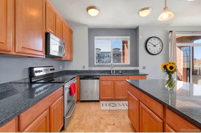 kitchen with brown cabinetry, dark stone counters, appliances with stainless steel finishes, hanging light fixtures, and a sink