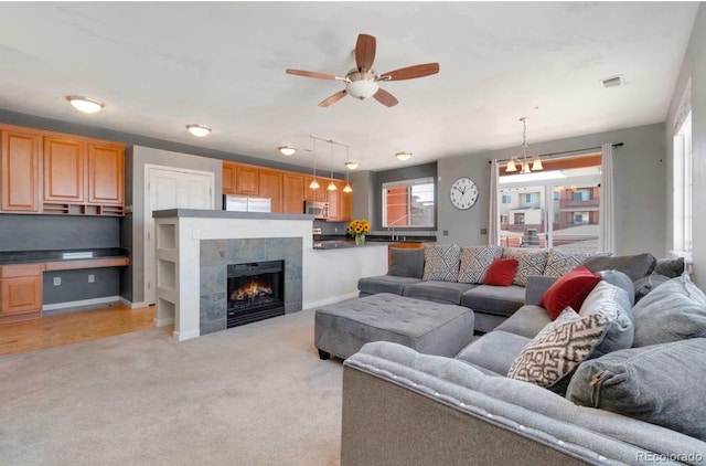 living area featuring light colored carpet, a fireplace, a ceiling fan, baseboards, and built in desk