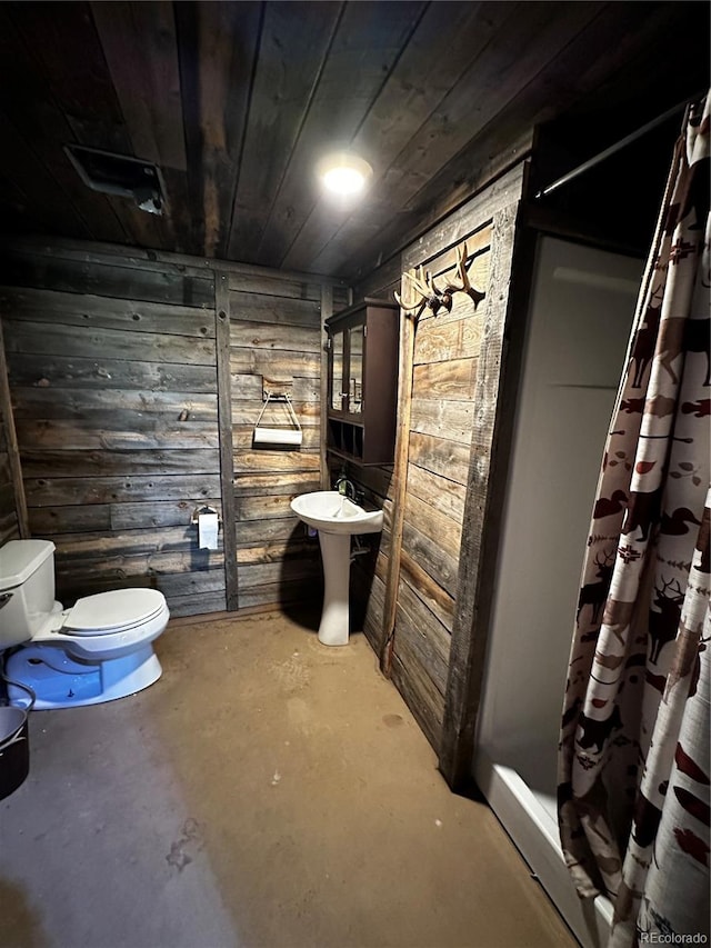 interior space featuring curtained shower, wooden walls, toilet, and concrete flooring