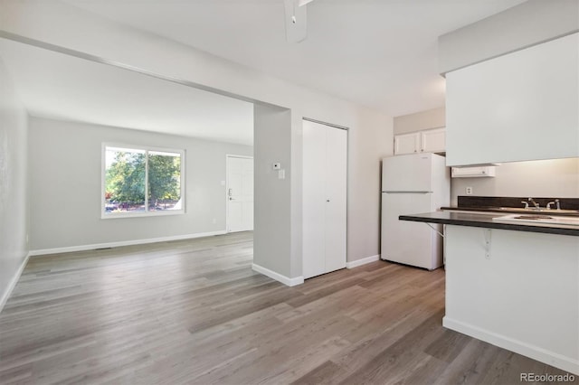 kitchen featuring white cabinetry, sink, a kitchen bar, white refrigerator, and light hardwood / wood-style floors