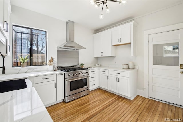 kitchen with wall chimney range hood, high end range, light hardwood / wood-style floors, white cabinetry, and light stone counters