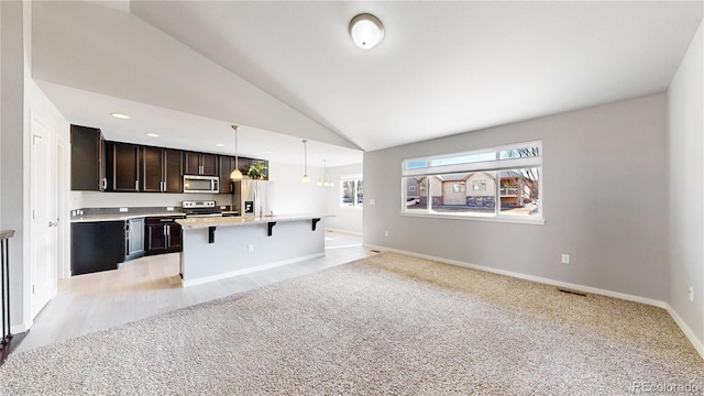 kitchen featuring a breakfast bar area, stainless steel appliances, light countertops, open floor plan, and vaulted ceiling