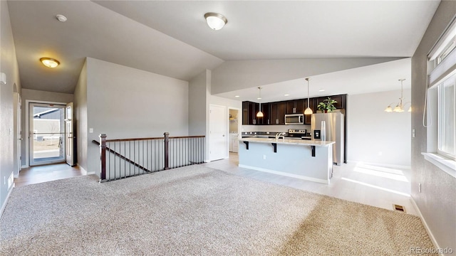 interior space featuring stainless steel appliances, a kitchen breakfast bar, vaulted ceiling, dark brown cabinets, and light countertops