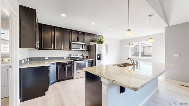 kitchen featuring appliances with stainless steel finishes, a sink, light wood finished floors, and light stone countertops