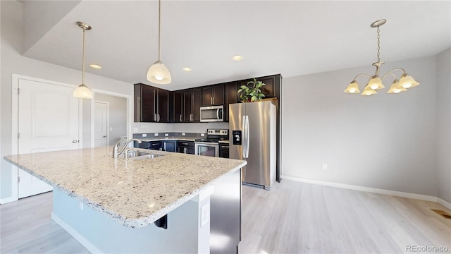 kitchen featuring appliances with stainless steel finishes, light wood-type flooring, a sink, and light stone counters