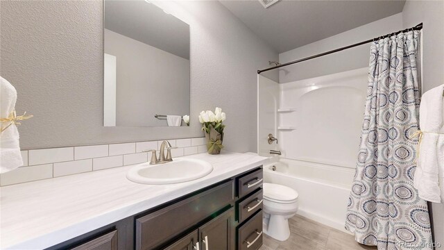 bathroom with a textured wall, shower / bath combo, vanity, and toilet