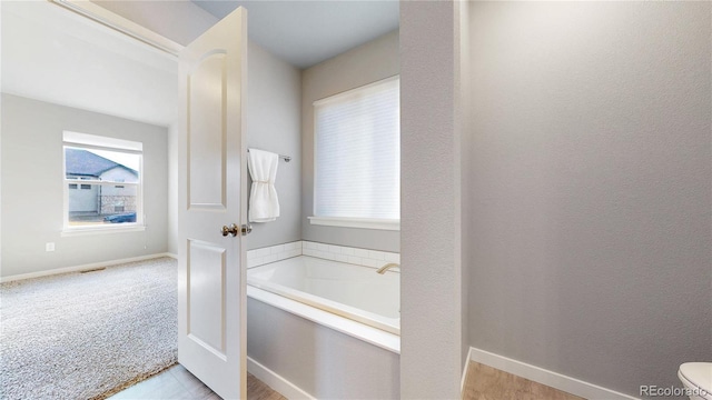 bathroom featuring a garden tub, a wealth of natural light, and baseboards