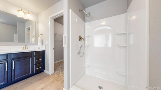 bathroom with wood finished floors, a spacious closet, walk in shower, vanity, and backsplash