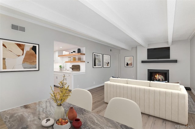 living room featuring sink, beamed ceiling, and light hardwood / wood-style floors