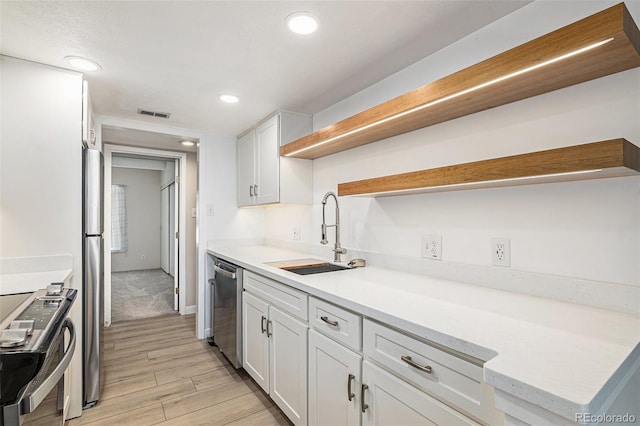 kitchen with appliances with stainless steel finishes, light hardwood / wood-style floors, white cabinetry, and sink