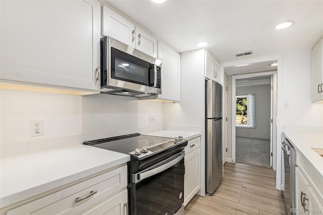 kitchen with stainless steel appliances, light hardwood / wood-style floors, and white cabinetry