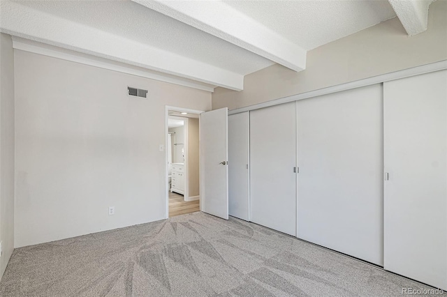 unfurnished bedroom featuring light carpet, beam ceiling, a closet, and a textured ceiling