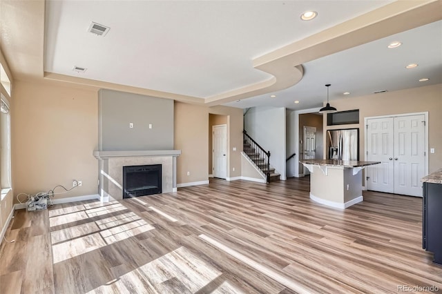 4625 Walden Ct, Denver, CO 80249 - unfurnished living room featuring a tray ceiling, stairs, light wood-style flooring, baseboards, and recessed lighting