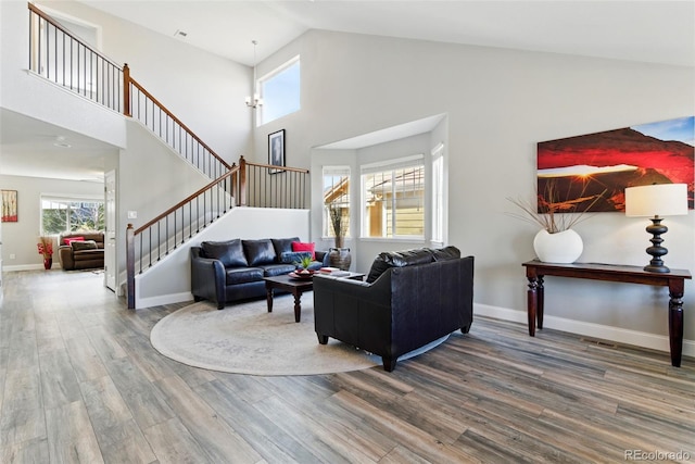 living area with stairway, baseboards, high vaulted ceiling, and wood finished floors