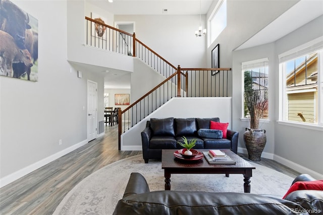 living room featuring stairway, an inviting chandelier, baseboards, and wood finished floors