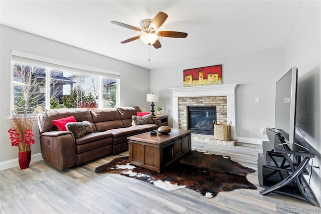 living room featuring baseboards, a brick fireplace, light wood-style flooring, and a ceiling fan