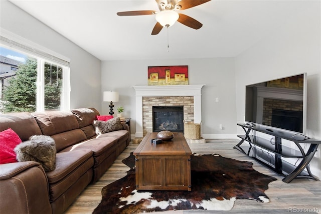 living area with a fireplace, baseboards, light wood-style floors, and a ceiling fan