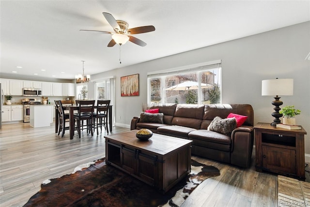 living area with recessed lighting, baseboards, ceiling fan with notable chandelier, and light wood finished floors