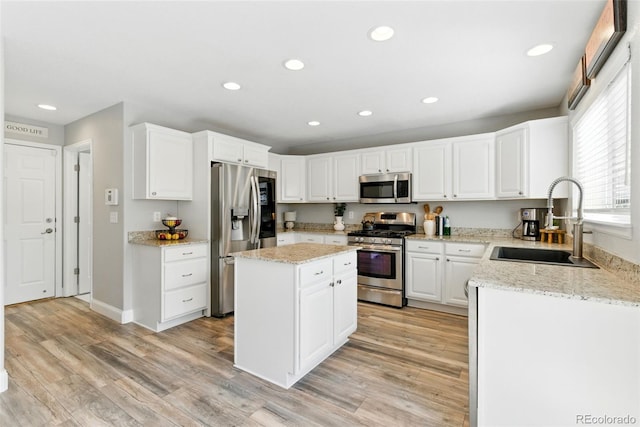 kitchen with light wood finished floors, appliances with stainless steel finishes, a center island, and a sink