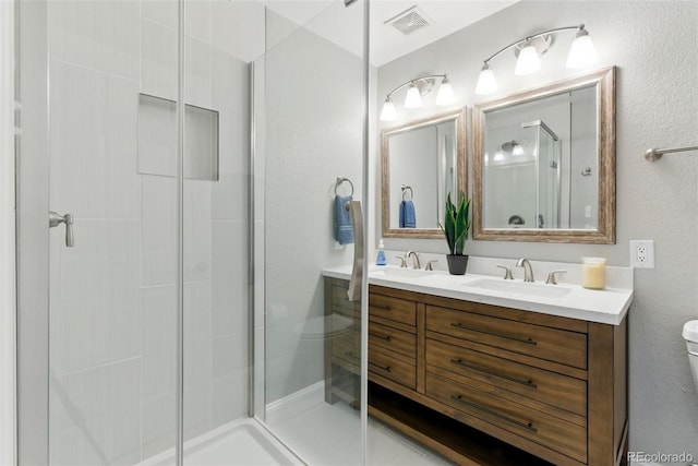 full bath with visible vents, toilet, a stall shower, a sink, and double vanity