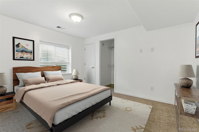 bedroom with a spacious closet, baseboards, visible vents, and light carpet