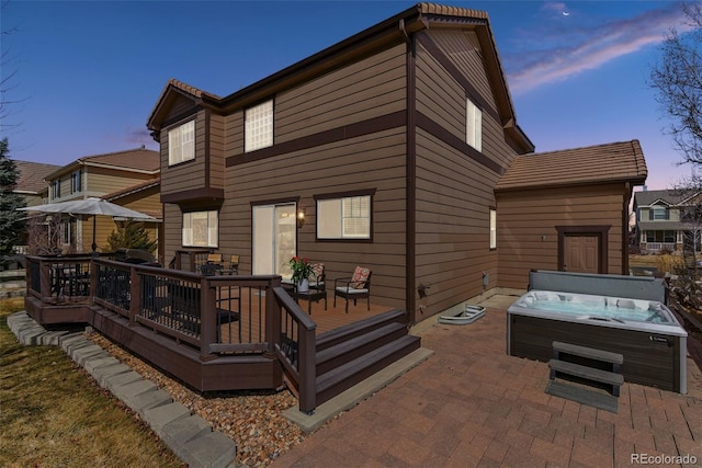 back of property at dusk with a wooden deck, a patio area, and a hot tub