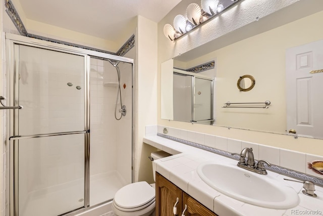 bathroom featuring a shower with door, vanity, and toilet