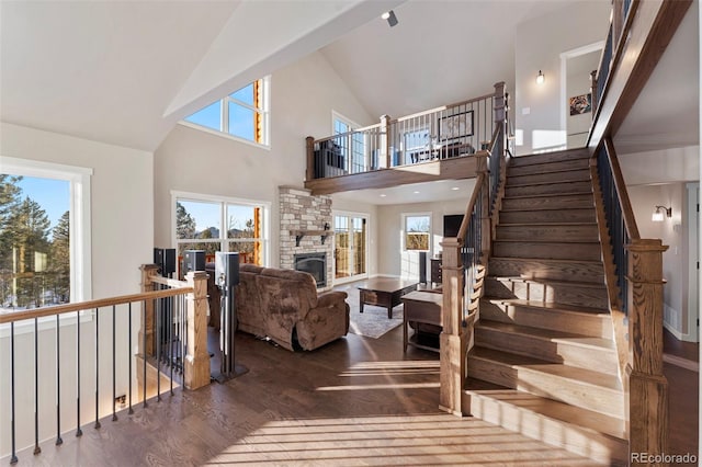 stairway with hardwood / wood-style floors, high vaulted ceiling, a stone fireplace, and plenty of natural light