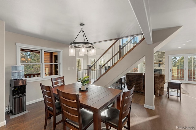 dining room featuring beam ceiling, an inviting chandelier, a stone fireplace, and dark wood-type flooring