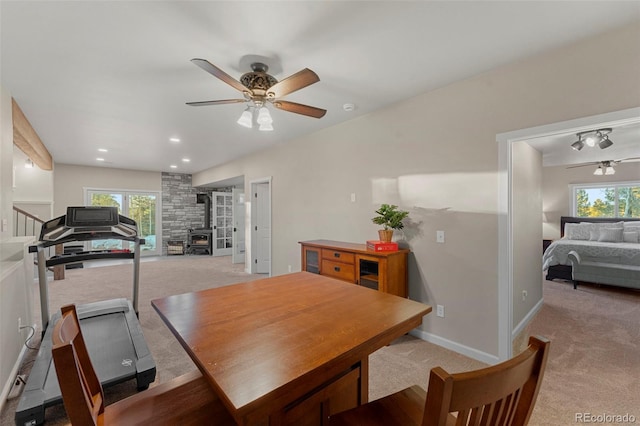 dining space with ceiling fan, light colored carpet, and a wood stove