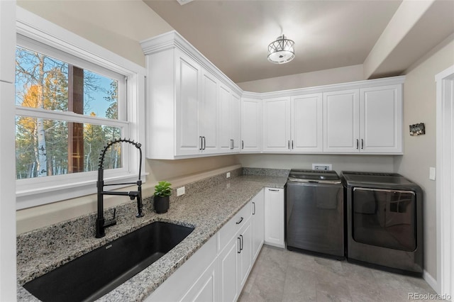 clothes washing area with washing machine and clothes dryer, sink, and cabinets