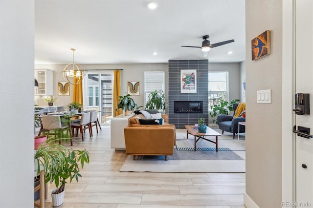 living room with ceiling fan with notable chandelier, recessed lighting, a tile fireplace, and light wood-style flooring