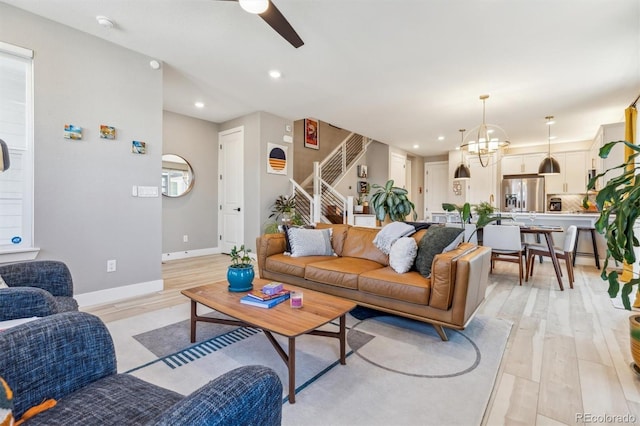 living area featuring light wood-type flooring, baseboards, recessed lighting, stairway, and ceiling fan with notable chandelier