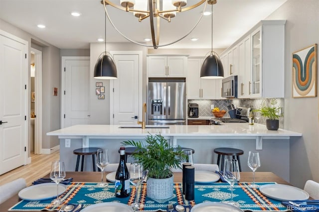 kitchen featuring glass insert cabinets, light countertops, backsplash, stainless steel appliances, and a sink