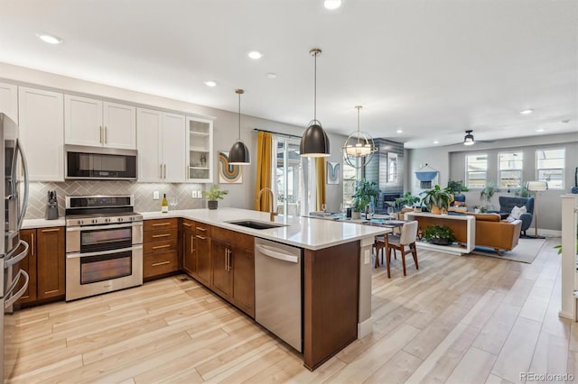 kitchen with a peninsula, appliances with stainless steel finishes, light countertops, a sink, and open floor plan