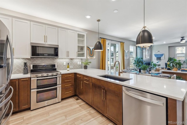 kitchen with a sink, light wood-type flooring, appliances with stainless steel finishes, a peninsula, and white cabinetry